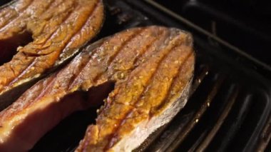 Kırmızı balıklı biftekler elektrikli ızgarada kızartılır. İştah açıcı pişmiş kahverengi, sulu somon parçaları. Sağlıklı beslenme. Omega 3 doymamış yağ asitleri. Protein yiyeceği. Yan görüş. Kamera hareketi