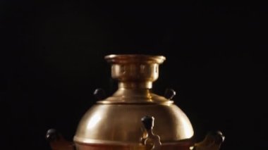 Kameranın tepeden tırnağa hareketi, eski bir bronz semaver, siyah bir arkaplanda karanlık bir odada bir masanın üzerinde duruyor ve evde çay için su kaynatmak için kullanılıyor.