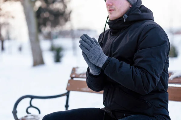 The guy in gloves warms his hands. The guy warms his hands. Hands in gray winter gloves. The palm with the glove in the snow.The guy in gloves warms his hands. The guy warms his hands. Hands in gray winter gloves. The palm with the glove in the snow.