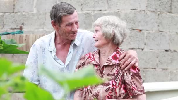 Abuelos ancianos sentados en el banco el día de verano sonriéndose el uno al otro — Vídeo de stock