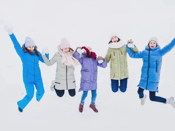 Радостные девушки прыгают рука об руку зимой на прогулке. Модная зимняя одежда — стоковое фото