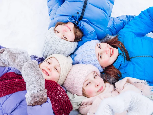 Un gruppo di bambini gioiosi in imballaggi luminosi e cappelli lavorati a maglia in inverno giacciono sulla neve e alzano lo sguardo — Foto Stock