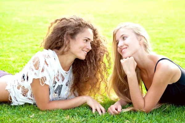 Duas belas garotas com cabelos longos encaracolados estão na grama em um dia de verão. Fotografias De Stock Royalty-Free