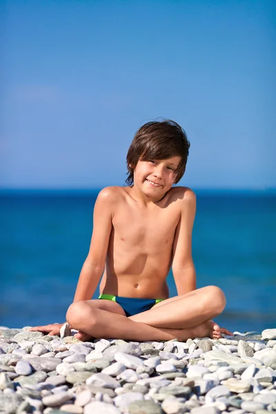 Schöner Junge sitzt am Strand — Stockfoto