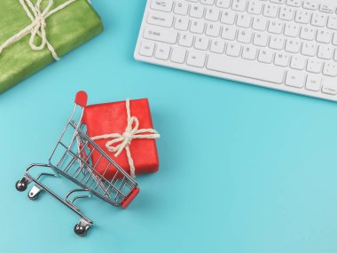 Alışveriş arabasında bilgisayar klavyeli kırmızı hediye kutusu ve mavi arka planda fotokopi alanı olan yeşil hediye kutusu. İnternetten alışveriş ve Noel tatili konsepti.