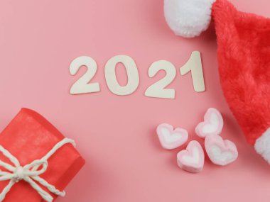 Noel şapkası, hediye kutuları ve kalp şeklinde şekerlemelerle pembe arka planda 2021 numaralı ahşabın üstü ya da düzlüğü..