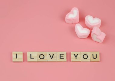Üst ya da düz tahta harfler. Seni seviyorum. Pembe arka planda kalp şeklinde şekerlemeler. Sevgililer günü ve aşk konsepti.