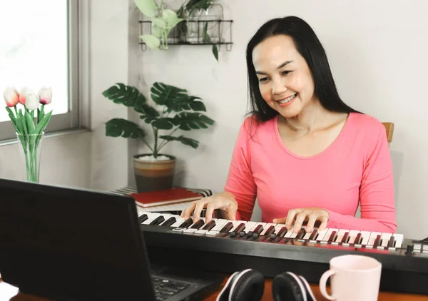 Portrait of Asian woman learning music lesson online , playing piano and looking at  computer notebook.  Teaching or learning online, social distancing and new normal.