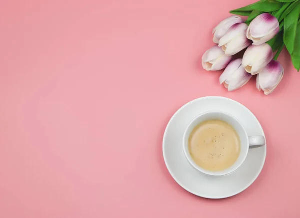 Top view or flat lay of coffee cup  on pink background with tulip flower bouquet. Copy space.