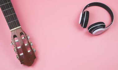 Üst ya da düz akustik gitar ve pembe arka planda fotokopi alanı olan beyaz kulaklıklar. Müzisyen, eğlence ve çevrimiçi müzik öğrenme kavramı.