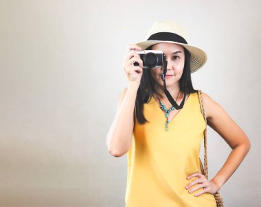 Sarı kolsuz gömlek ve şapka giyen Asyalı kadın turist portresi, kameraya bakarak gözlerini kapatıyor..