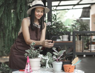 Evinin bahçesinde çalışan Asyalı kadın bahçıvanın portresi. İnternette satmak için saksıdaki bitkisinin fotoğrafını çekiyor..