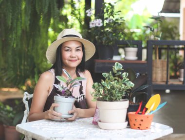 Evinin bahçesinde çalışan Asyalı kadın bahçıvanın portresi. Elinde bitki saksısı var, gülümsüyor ve kameraya bakıyor. Bahçe işleri konsepti.