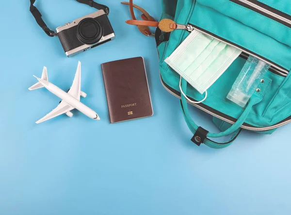 Top view or flat lay of traveling accessories with airplane model and medical face mask and alcohol sanitizer gel on blue background. Traveling during covid-19 epidemic.