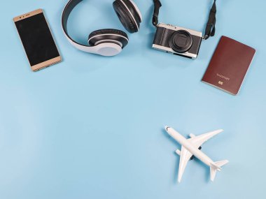 Mavi arka planda uçak modeli, pasaport, kamera, kulaklık ve cep telefonu var. Seyahat aksesuarları konsepti.