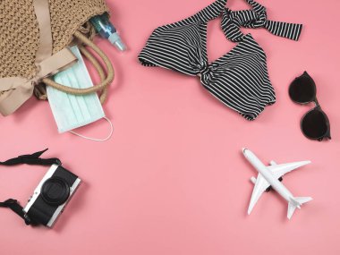 Seyahat aksesuarları, tıbbi maske ve pembe arka planda dokuma poşetinde alkol dezenfektanı. Covid-19 ve yeni normaller sırasında seyahat etmek.