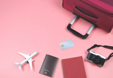 Üst ya da düz uçak modeli, kırmızı günlük, kamera pasaportu, kredi kartı ve pembe arka planda pembe bavul. Seyahat konsepti.