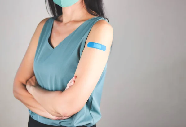Aşılanmış Asyalı kadının yeşil kolsuz tişörtü ve bez maskesiyle Coronavirus aşısı yaptırdıktan sonra kolunda bandaj olan görüntüsü..