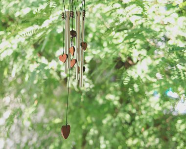 Wind chime with wooden herat shape hanging in the garden, green leaves background. clipart