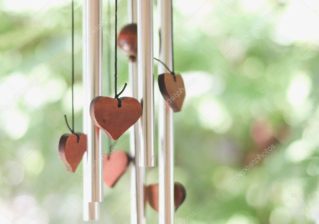 Close up image of wooden hearts hanging with wind chime with green garden background.