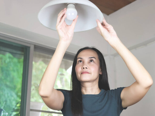 Asian woman  changing light bulb in her house. 