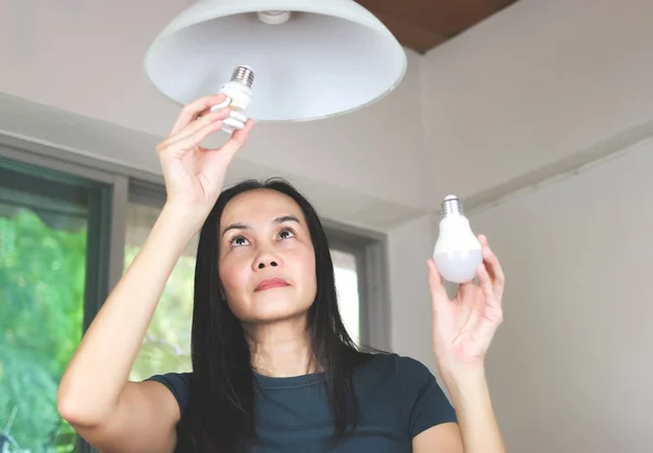Asyalı kadın ampulü değiştiriyor, spiral ampulden LED ampulüne. Kadın gözlerine odaklan..