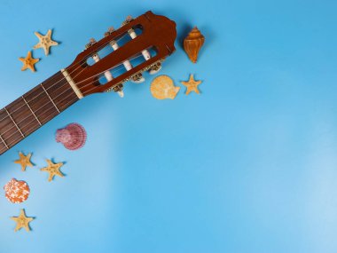 Mavi arka planda deniz kabukları ve deniz yıldızları olan akustik gitarın üst görüntüsü veya düz yatağı, kopyalama alanı. Yaz sahili akustik müzik arka planı.