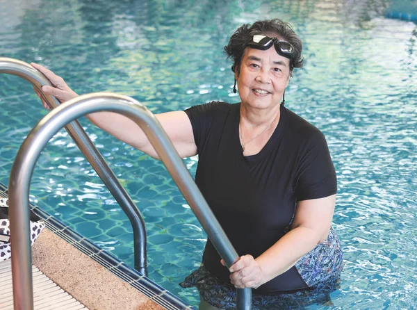 Portrait of happy and healthy Asian senior woman wearing swimming wear and goggles, standing at stair, smiling and looking at camera. Elderly sports and active lifestyle.