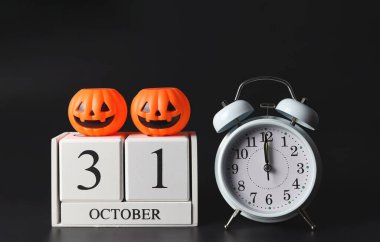 Beyaz antika çalar saatin ön görüntüsü saat 12 yönünde ve tahta takvim 31 Ekim 'de siyah arka planda plastik cadılar bayramı balkabakları var. Cadılar Bayramı partisi konsepti.