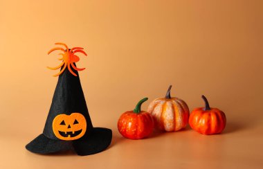 Cadılar Bayramı cadı şapkasının ön görüntüsü kabak kafasıyla süslenmiş ve turuncu arka planda plastik balkabağı olan örümcek. Cadılar Bayramı kostüm partisi.