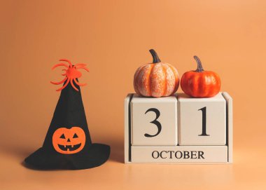 31 Ekim 'de üzerinde balkabağı ve turuncu arka planda balkabağı kafası ve örümcekle süslenmiş cadılar bayramı cadı şapkası olan ahşap takvimin ön görüntüsü. Cadılar Bayramı kostüm.