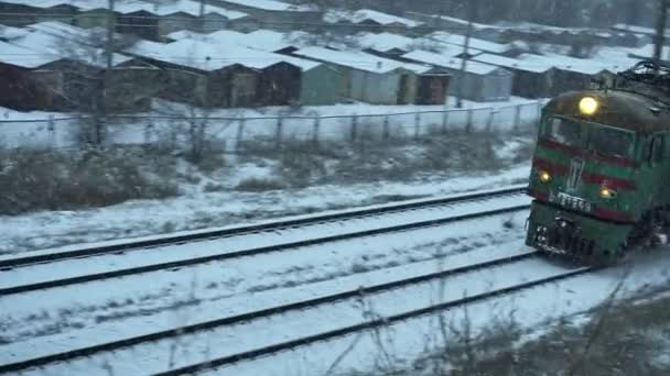 ZAPOROZHYE, UKRAINE - FEBRUARI 18, 2021: oude locomotief met geladen wagons passeert per spoor in de wind van zware sneeuwval, goederentrein — Stockvideo