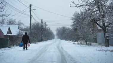 ZAPOROZHYE, UKRAINE - 22 Şubat 2021: Paketleri olan bir adam kışın caddelerden geçer güzel kar manzarası düşer