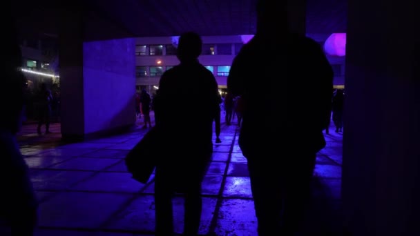 ZAPOROZHYE, UKRAJINA - 07. ZÁŘÍ 2020: tmavé siluety lidí míjejících se proti modrému světlu lamp — Stock video