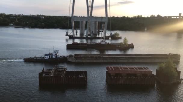Een groot vrachtschip zonder lading passeert 's avonds bij zonsondergang langs een brede rivier bij de bouw van bruggen — Stockvideo