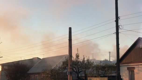 Oheň v soukromém domě hustý kouř stoupá nad střechy na jasném jarním nebi — Stock video