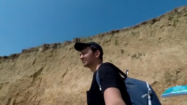 Um viajante anda ao longo da praia com um penhasco — Vídeo de Stock