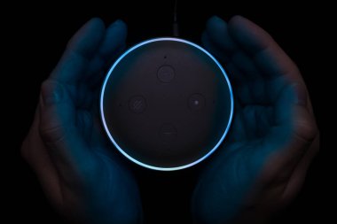 Aydınlatılmış Amazon Yankı Noktası akıllı hoparlörü kullanan kişi.