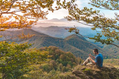 Uçurumun kenarında oturan ve telefonuna bakan bir adam. Macera yalnız seyahat yaşam tarzı. Seyahat tutkusu macera konsepti. Aktif hafta sonu tatili vahşi doğa. 