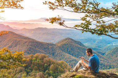 Uçurumun kenarında oturan ve telefonuna bakan bir adam. Macera yalnız seyahat yaşam tarzı. Seyahat tutkusu macera konsepti. Aktif hafta sonu tatili vahşi doğa. 