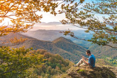 Uçurumun kenarında oturan ve telefonuna bakan bir adam. Macera yalnız seyahat yaşam tarzı. Seyahat tutkusu macera konsepti. Aktif hafta sonu tatili vahşi doğa. 
