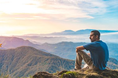 Uçurumun kenarında oturan bir adam etrafındaki güzel ve engebeli araziye bakıyor. Macera yalnız seyahat yaşam tarzı. Seyahat tutkusu macera konsepti. Aktif hafta sonu tatili vahşi doğa. 