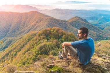 Uçurumun kenarında oturan bir adam etrafındaki güzel ve engebeli araziye bakıyor. Macera yalnız seyahat yaşam tarzı. Seyahat tutkusu macera konsepti. Aktif hafta sonu tatili vahşi doğa. 