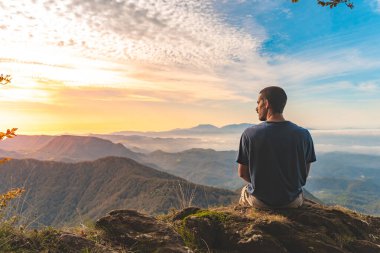 Uçurumun kenarında oturan bir adam etrafındaki güzel ve engebeli araziye bakıyor. Macera yalnız seyahat yaşam tarzı. Seyahat tutkusu macera konsepti. Aktif hafta sonu tatili vahşi doğa. 