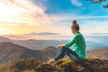 Uçurumun kenarında oturan bir kadın gezgin dağlara bakıyor. Macera yalnız seyahat yaşam tarzı. Seyahat tutkusu macera konsepti. Aktif hafta sonu tatili vahşi doğa. Sonbahar sonbahar ormanı.