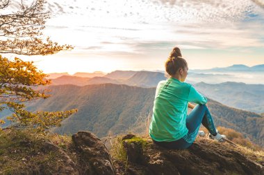 Uçurumun kenarında oturan bir kadın gezgin dağlara bakıyor. Macera yalnız seyahat yaşam tarzı. Seyahat tutkusu macera konsepti. Aktif hafta sonu tatili vahşi doğa. Sonbahar sonbahar ormanı.