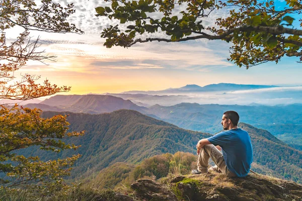 Uçurumun kenarında oturan bir adam etrafındaki güzel ve engebeli araziye bakıyor. Macera yalnız seyahat yaşam tarzı. Seyahat tutkusu macera konsepti. Aktif hafta sonu tatili vahşi doğa. 
