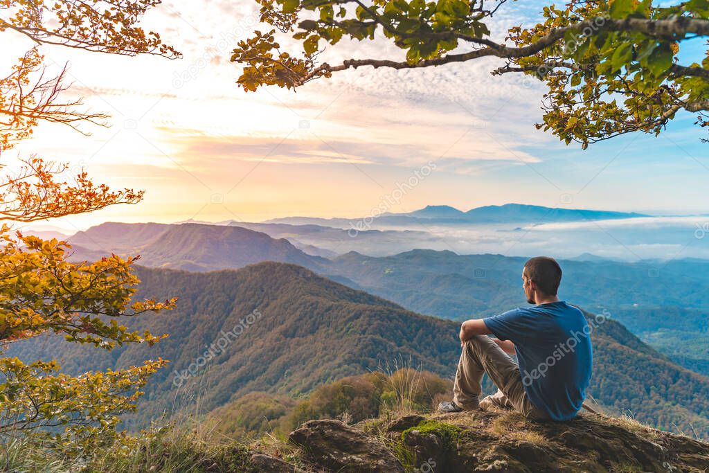 Man sitting on a edge of a cliff and looking at beautiful and rough terrain around him. Adventure solo traveling lifestyle. Wanderlust adventure concept. Active weekend vacations wild nature outdoor. 