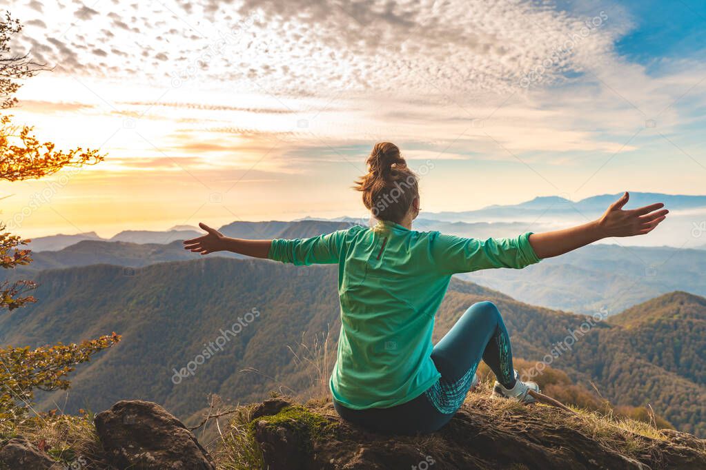 Woman traveler sitting in the edge of a cliff looking the mountains. Adventure solo traveling lifestyle. Wanderlust adventure concept. Active weekend vacations wild nature outdoor. Autumn fall forest.