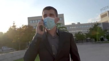 Klasik takım elbiseli iş adamlarına yakın çekim yapmak açık havada akıllı telefon kullanmaktır. Ofis binasında cep telefonuyla iş görüşmesi yapıyorum. Koronavirüs salgını koruyucu yüz maskesi.